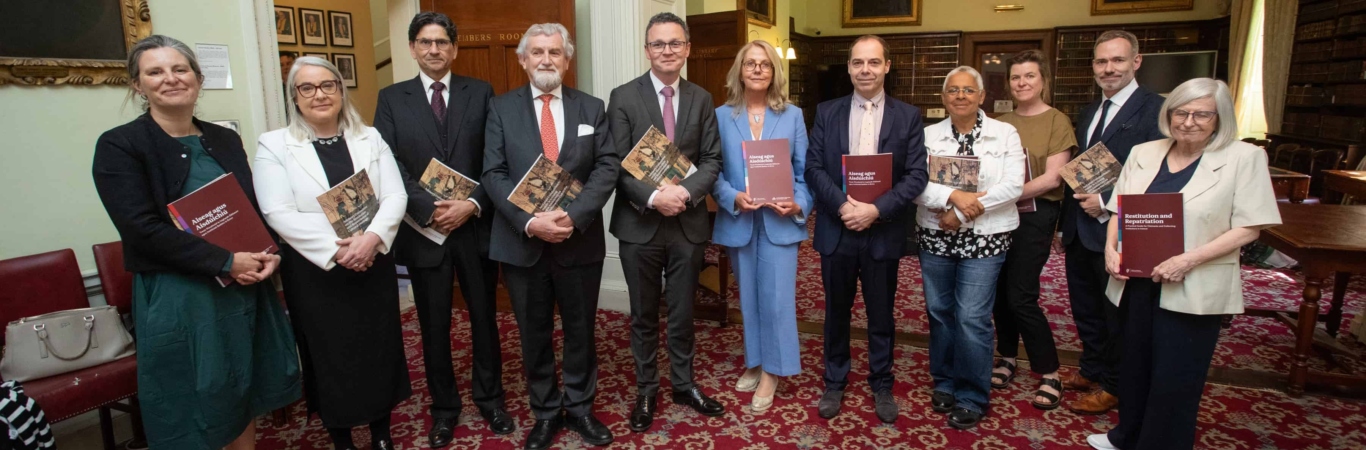 Eleven people in a library holding copies of the Advisory Committee on the Restitution and Repatriation of Cultural Heritage report.